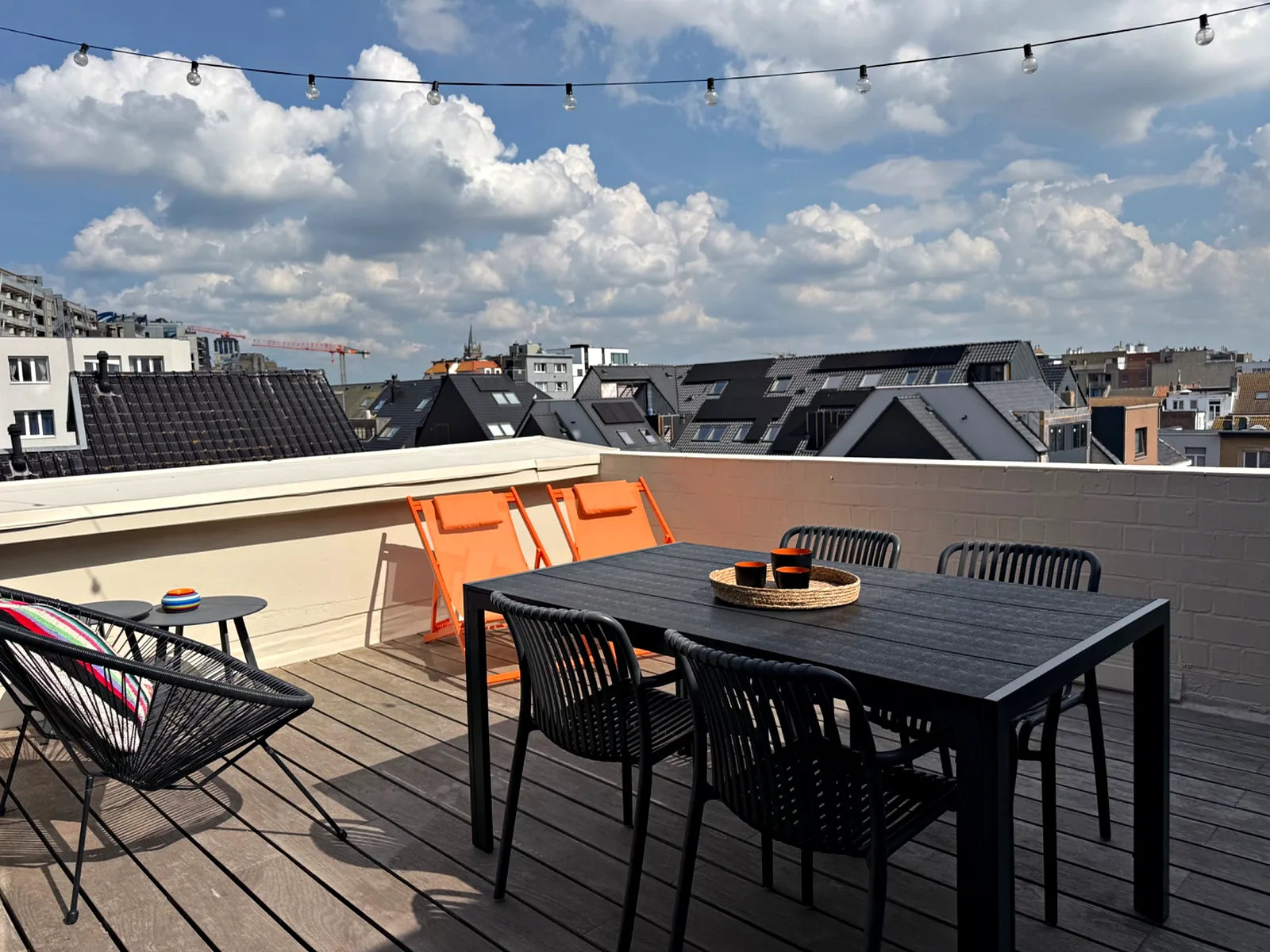 Table et transats orange sur la terrasse, sous les guirlandes, avec vue sur les toits